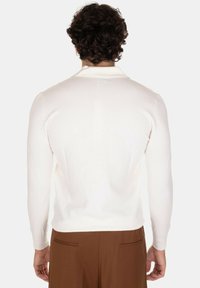 Maglione a maglia di colore crema con maniche lunghe e scollo rotondo, mostrato da dietro. Tessuto liscio, design aderente. Pantaloni marroni visibili.
