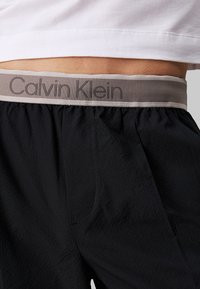 Shorts neri in tessuto testurizzato, con una cintura in vita grigia con il logo Calvin Klein. Cintura elastica per una vestibilità e comfort ottimali.
