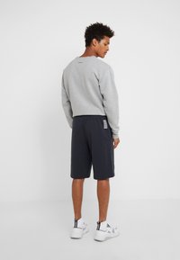 Felpa grigia con collo rotondo, abbinata a pantaloni corti blu scuro con una tasca laterale e strisce bianche. Indossata con sneakers bianche.