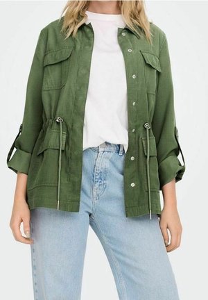 Grøn letvægtsjakke med to frontlommer, knaplukning og justerbar snor i taljen. Sammen med en hvid skjorte og blå jeans.