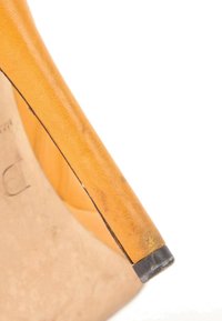 Gros plan sur la pointe du talon d’une chaussure à talons haute jaune usée avec un embout en caoutchouc noir sur fond blanc.