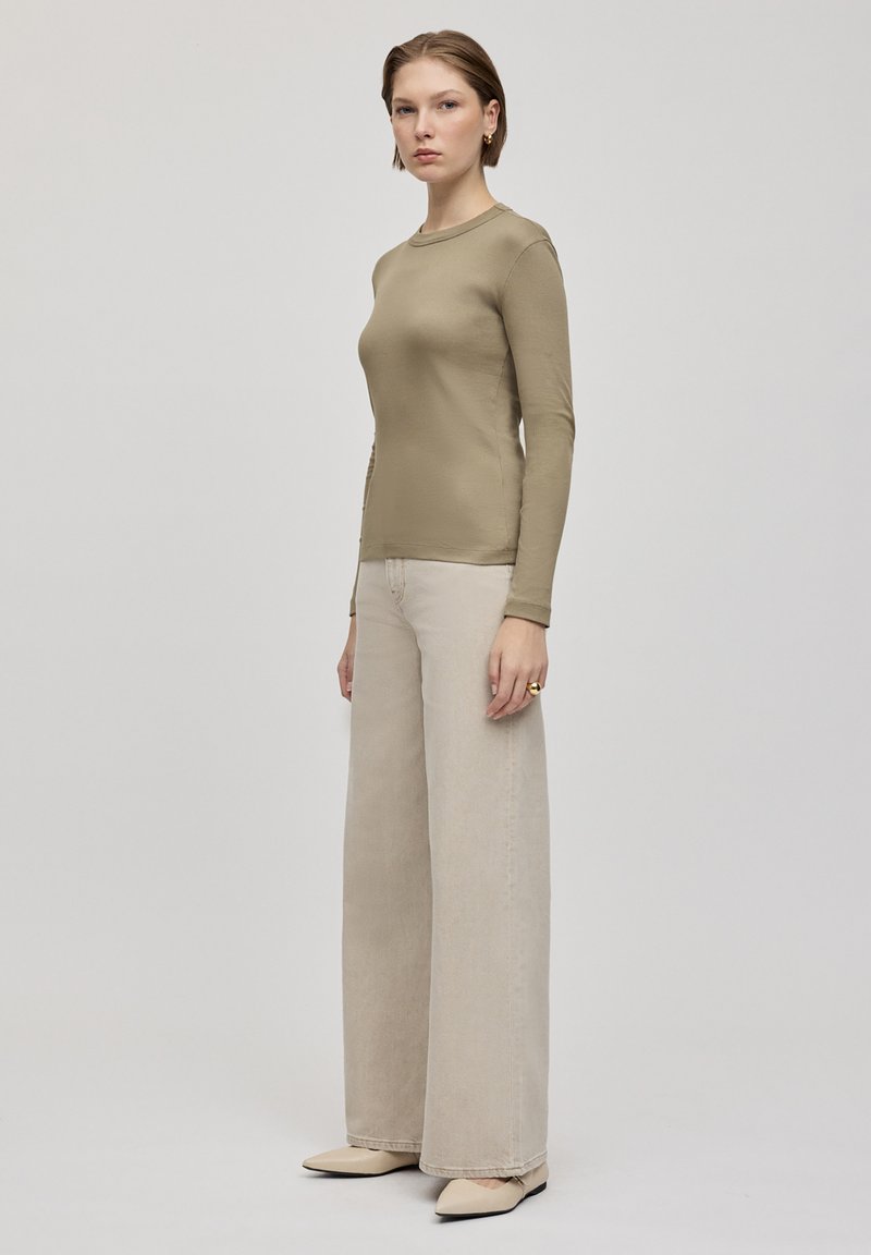 Lichtolijfkleurig, langemouwen top gecombineerd met ruime beige jeans en beige flats. De outfit heeft een getailleerde silhoutte en een minimalistisch ontwerp.