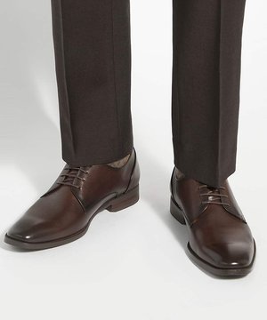 Donkerbruine leren nette schoenen met veters, gedragen met donkere broeken tegen een effen lichte achtergrond.