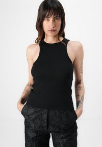 Black ribbed tank top with a high neckline and sleeveless design, paired with textured black trousers featuring a floral pattern.