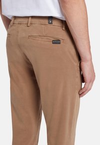 Pantaloni di cotone color beige con una texture liscia, dotati di due tasche posteriori, un'etichetta e una vestibilità su misura.