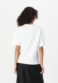 T-shirt en coton blanc à manches courtes et coupe décontractée ; présente un col rond et une texture lisse, affiché de dos.