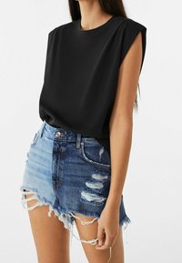 Top nero a maniche corte in tessuto liscio, abbinato a pantaloncini di jeans strappati con bordi sfrangiati e sfumatura dal blu chiaro al blu scuro.