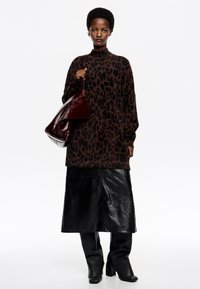 Suéter de estampado de leopardo en marrón oscuro, combinado con una falda de cuero negra y botas de caña alta a juego, llevando un bolso de cuero rojo oscuro.