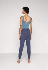 Lys blå topp med lav rygg, kombinert med marineblå joggebukser med elastiske mansjetter. Stoffet ser mykt og uformelt ut.