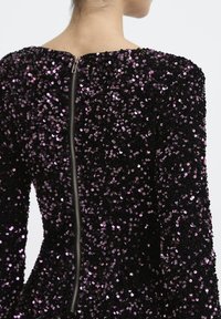 Musternäidises must kleit, millel on lilla sädelused, laeva kaelus ja tõmblukuga sulgemine taga. Tekstuuriga pind läikivate aktsentidega.