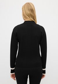 Maglione nero con colletto, maniche lunghe caratterizzate da accenti a righe bianche e nere ai polsini e un design aderente. Texture liscia.