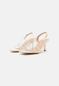 Sandales à talons aiguilles blanches à lanières avec un bout pointu, dotées d'un talon transparent fin, d'une bride de cheville et d'une semelle intérieure beige lisse.