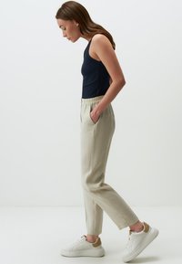 Canottiera a coste navy, pantaloni crema con vita elastica e sneakers bianchi con dettagli beige; in esposizione in profilo laterale su uno sfondo neutro.