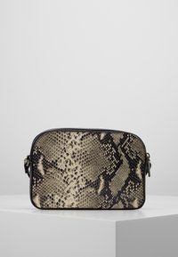 Obdélníková crossbody taška s černým a béžovým hadím vzorem, černým zipem a nastavitelným bočním popruhem, vystavená na bílém podstavci.