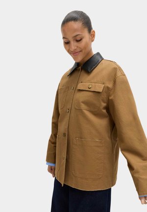 Chaqueta marrón con cuello de cuero negro, bolsillos delanteros, botones de presión y corte holgado. Material de algodón con textura suave.