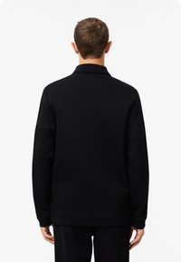 Sudadera negra con cuello, que presenta mangas largas y un corte holgado. Textura suave con un diseño minimalista, sin patrones o acentos notables.