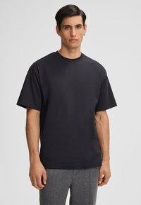 Zwarte katoenen T-shirt met een relaxte pasvorm, korte mouwen en een ronde halslijn. Draagt met grijze sportbroek. Gladde textuur.