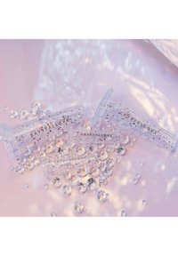 Fermagli per capelli trasparenti, pieni di glitter, con la scritta "CRYSTALLOVE" in oro, sparsi tra gioielli trasparenti, su uno sfondo rosa chiaro.