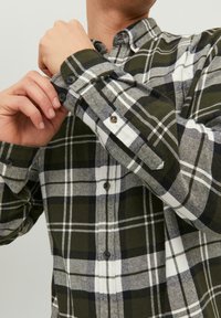 Camicia con bottoni caratterizzata da un motivo a quadri verde, nero e bianco. Realizzata in tessuto morbido con colletto e polsini abbottonati.
