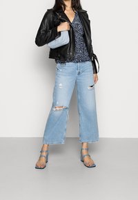 Zwarte leren jas, blauw gebloesd blouse, lichtblauwe tas, lichtblauwe wijde jeans met scheuren en blauwe sandalen met bandjes.