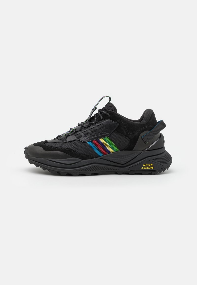 Baskets noires avec des bandes multicolores sur le côté et texte "NEVER ASSUME" en jaune sur la semelle près du talon.