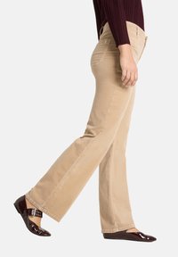 Pantalon en velours côtelé beige à coupe droite, associé à des ballerines bordeaux brillantes avec une bride décorative et une boucle.