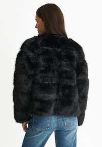 Black faux fur jacket with a textured, puffy design. Features a cropped cut and wide sleeves. Worn with blue denim jeans.