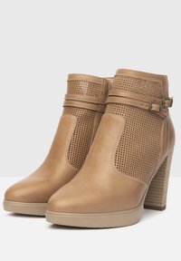 Bottines tan avec des côtés perforés, un accent de boucle et un talon empilé. Matériau en cuir lisse avec un bout rond et une texture subtile.