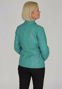 Türkise Lederjacke mit taillierter Passform, glatter Textur und Stehkragen, über schwarzen Hosen getragen, von hinten gezeigt.