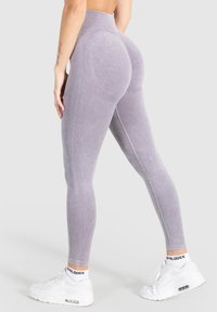 Leggings grises de cintura alta con una textura suave, presentando acentos acanalados y un ajuste moldeador. Combinados con zapatillas deportivas blancas y calcetines.