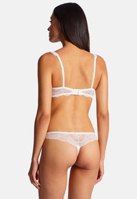Ensemble de lingerie en dentelle blanche avec un motif floral délicat. Le soutien-gorge possède des bretelles réglables et une fermeture à crochet ; le string offre des détails transparents.