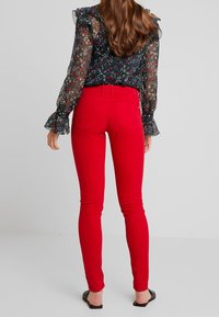 Jeans ajustados rojos con una textura suave y diseño de cinco bolsillos, combinados con una blusa oscura de flores con mangas rizadas.