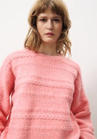Rosa gestrickter Pullover mit einem strukturierten Muster, mit Rundhalsausschnitt und langen Ärmeln, hergestellt aus weichem, flauschigem Material.