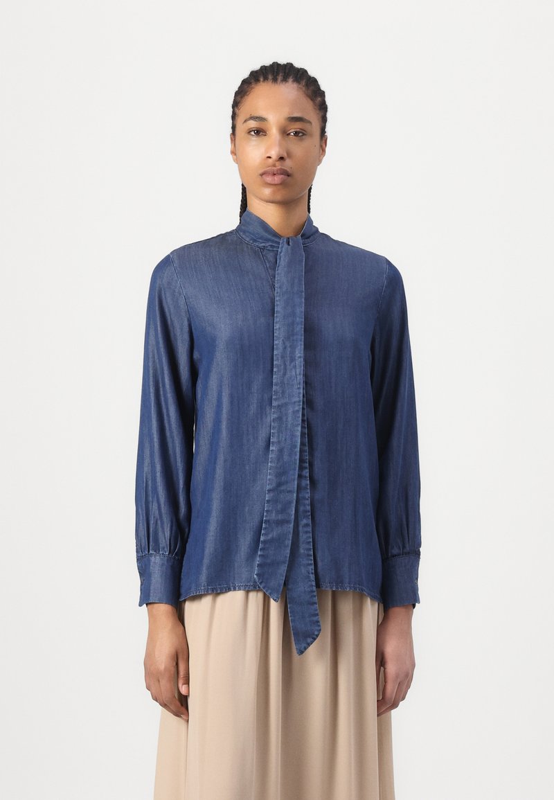 Denimhemd mit hohem Kragen, Bindeband vorne, langen Ärmeln und geknöpften Manschetten. Verfügt über eine glatte Textur in einem dunklen Blauton.