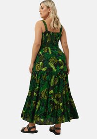Maxiklänning i grön och svart med ett lövmönster. Har en smockad bodice, tjocka band och en design med lager på kjolen. Bärs med svarta sandaler.