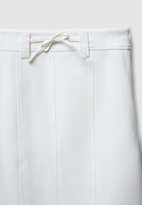 Pantalons blancs structurés avec une taille à cordon de serrage, présentant deux plis verticaux sur le devant et un tissu lisse et texturé.