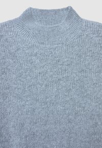 Pull en tricot gris clair avec un col haut, présentant un motif texturé de cercles entrelacés, en tissu doux et avec des coutures visibles.