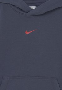 Námořnická modrá mikina s kapucí vyrobená z bavlněného směsového materiálu, s červeným logem Nike swoosh na hrudi a přední klokaní kapsou.