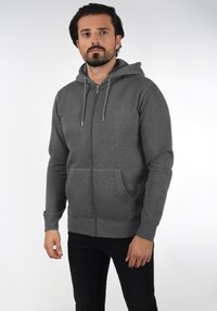 Grijze zip-up hoodie met een capuchon, voorzakken en lange mouwen. Kenmerkt zich door een soepel stoftextuur en een zilveren metalen rits.
