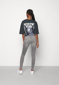 Camiseta negra de gran tamaño con un gráfico de "MYSTIC VIBE", combinada con jeans ajustados grises y zapatillas blancas. Textura suave y diseño casual.