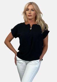 Czarna krótka bluzka z dekoltem w serek, z złotymi guzikami na ramionach, wykonana z teksturowanej tkaniny, w komplecie z białymi dopasowanymi spodniami.