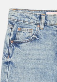 Jeans de mezclilla de un azul claro con una textura desgastada, que cuentan con detalles de cobre, cinco bolsillos y costuras contrastantes cerca de la cinturilla.