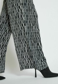 Black and white patterned wide-leg trousers with a geometric print, paired with black stiletto heel shoes. Smooth fabric texture.