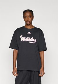 Μαύρο υπερμεγέθες t-shirt με ροζ λογότυπο «Adidas». Κοντά μανίκια, στρογγυλή λαιμόκοψη, κατασκευασμένο από απαλό βαμ�βάκι, σχεδιασμένο για καθημερινή χρήση.
