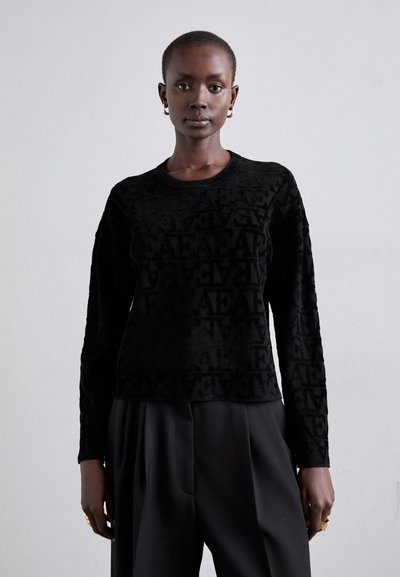 Maglione nero caratterizzato da un motivo testurizzato con lettere, maniche lunghe e collo rotondo, abbinato a pantaloni neri di taglio loose.