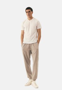 Biała koszulka z krótkim rękawem w połączeniu z jasnoszarymi spodniami dresowymi. Spodnie mają elastyczny pas i ściągacze na kostkach, noszone z beżowymi sneakersami.