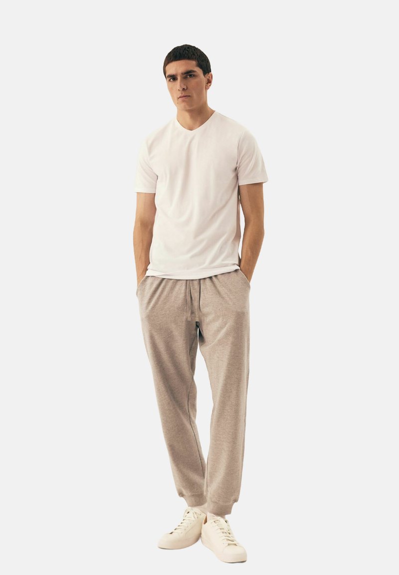 Biała koszulka z krótkim rękawem w połączeniu z jasnoszarymi spodniami dresowymi. Spodnie mają elastyczny pas i ściągacze na kostkach, noszone z beżowymi sneakersami.