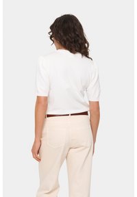 Top bianco a maniche corte con spalle a sbuffo, tessuto a maglia testurizzato, abbinato a pantaloni chiari e una cintura marrone in vita.
