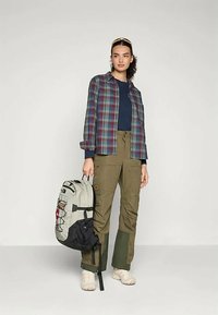 Raibais krekliņš ar pogām zilos un bordo toņos, tumši zila augšējā daļa, olīvu krāsas bikses ar kabatām, krēmkrāsas apavi un divkrāsains melns un pelēks mugursoma.