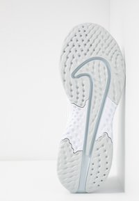 Biała podeszwa sportowego buta z teksturowanej gumy, z rowkami zapewniającymi przyczepność i zakrzywionym elementem designu w pobliżu pięty.